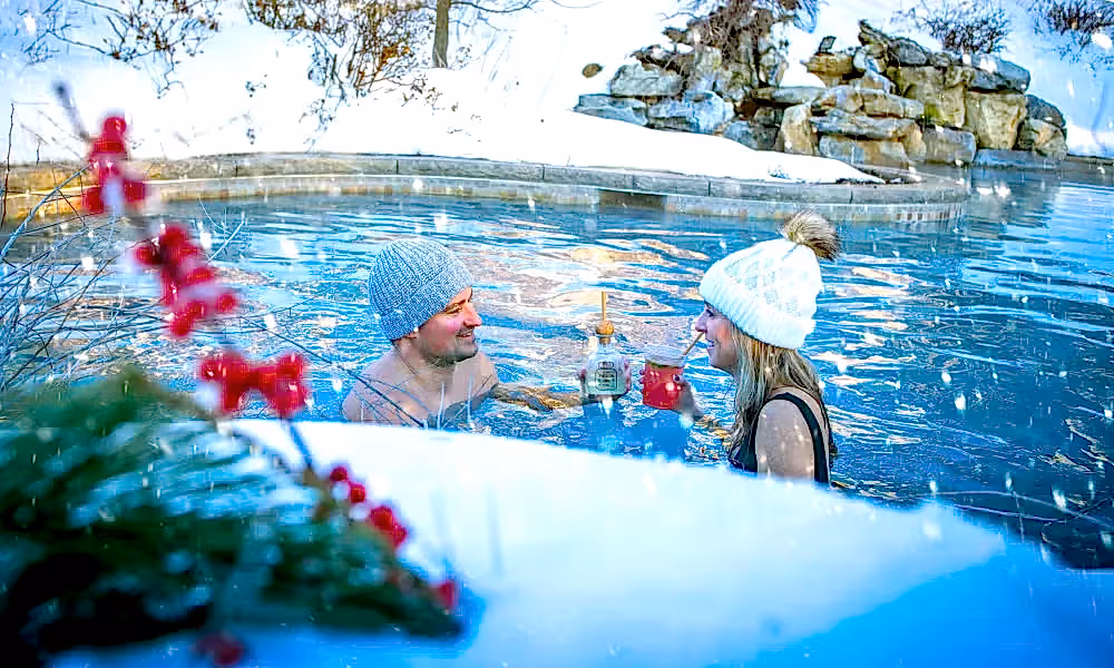 Couple drinks cocktails in outdoor snow pool.